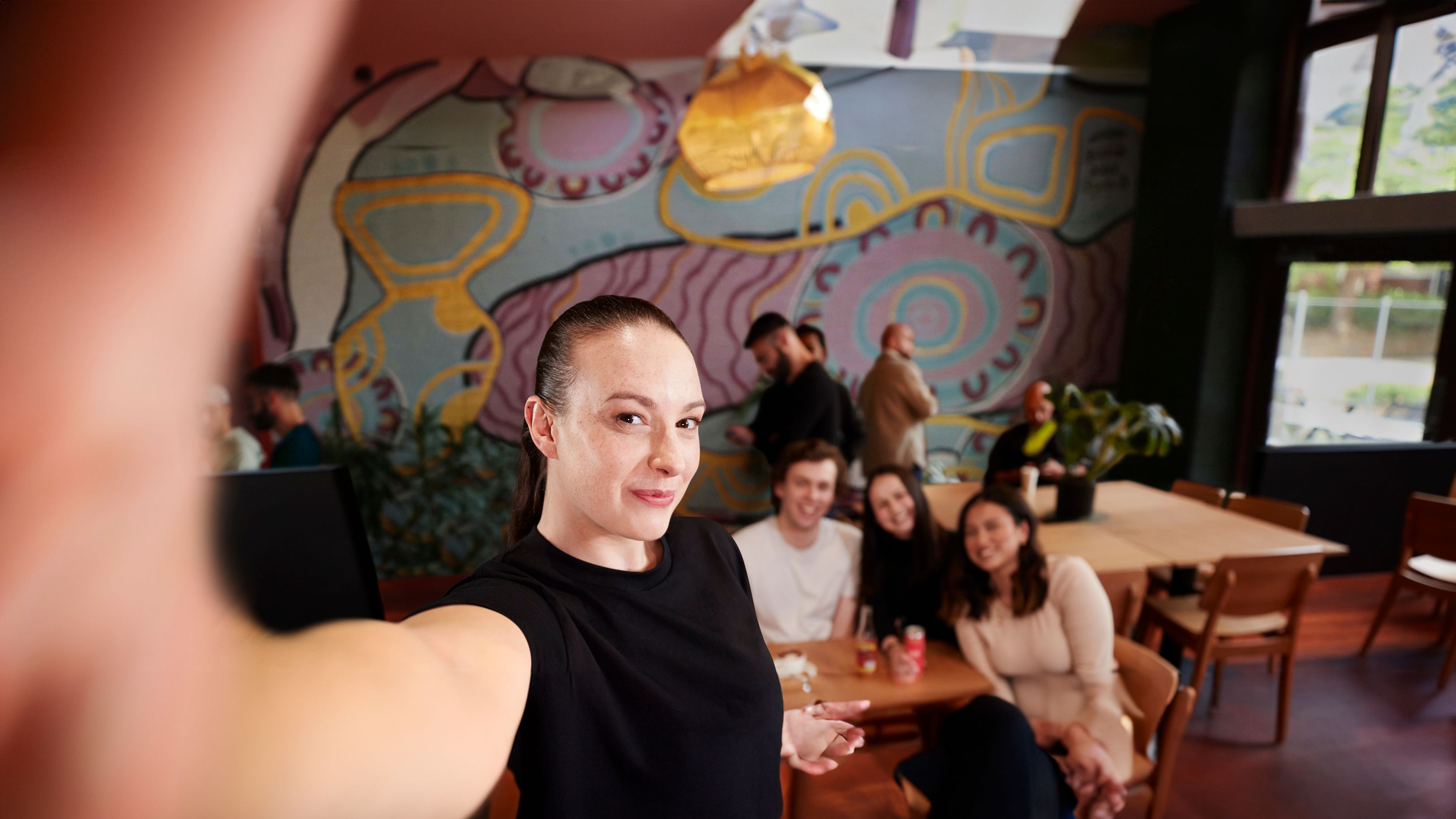 Young woman holding camera/phone taking a selfie with a group of people smiling behind her