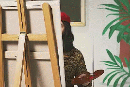 Man leans out from behind an easel to get perspective on what he is painting. Man leans out from behind an easel to get perspective on what he is painting.