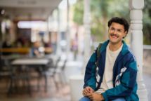  A student smiles while sitting outdoors on campus, enjoying a relaxed moment between classes.
