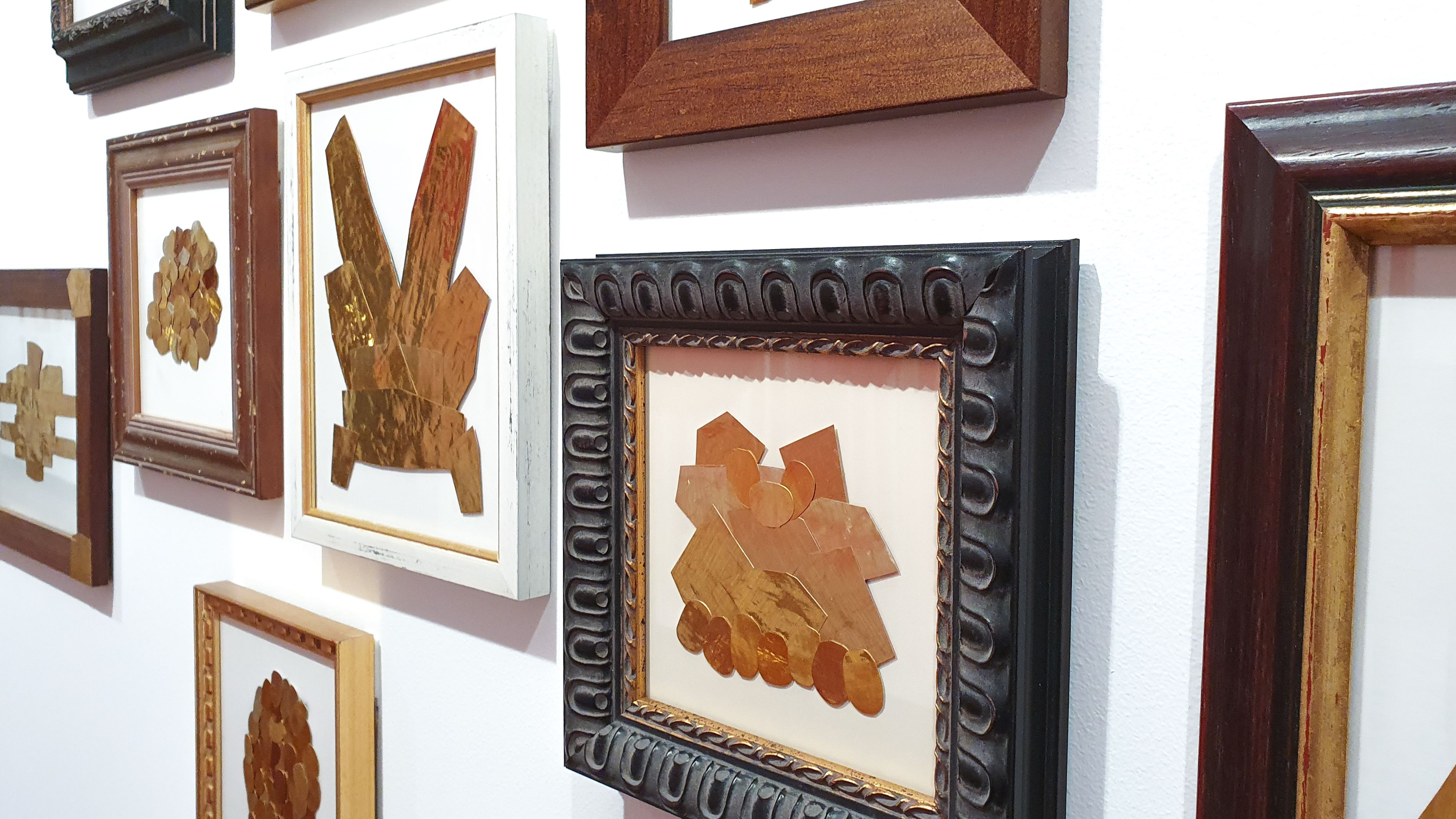 Gold Mine artwork Geometric shapes made from pieces of gold-coloured metal are displayed in an eclectic assortment of wooden frames and hung on a white wall in the Boroondara Town Hall Gallery
