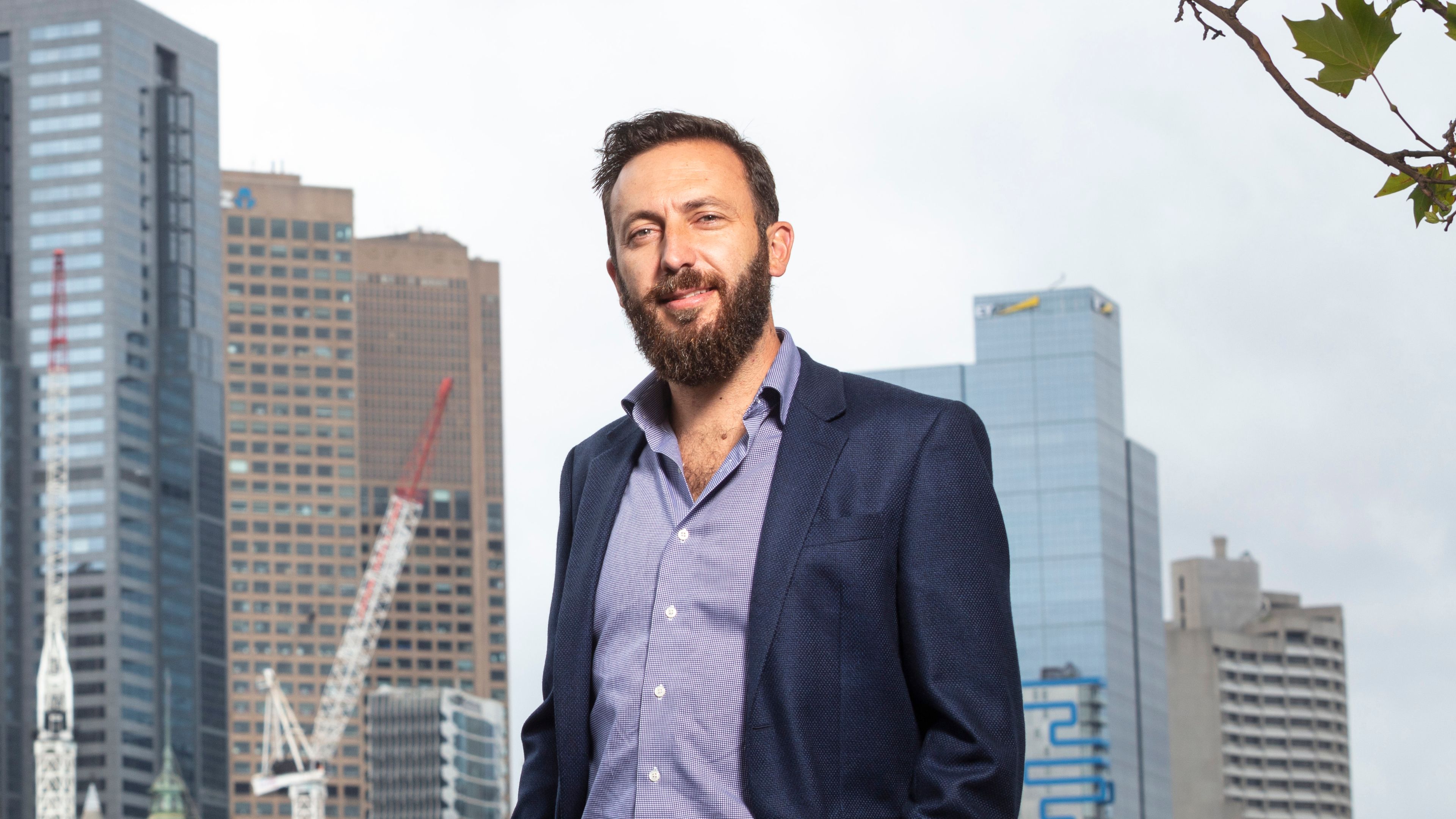 Peter Nguyen-Brown - 30 Years Young Mid-shot of Peter Nguyen wearing a blue suit jacket and smiling to camera with the Melbourne CBD in the background
