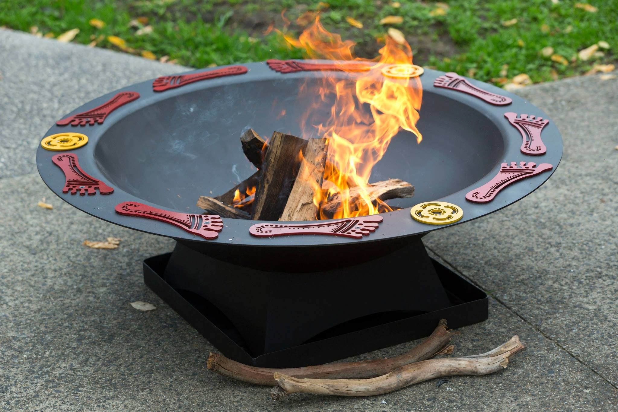 Fire pit at Reconciliation Action Plan launch 2014 A round, black fire pit with decorative red feet and yellow circle symbols around the edge and a fire burning inside.