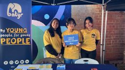 Three batyr student ambassadors at an on-campus stall, with one holding a sign that says “I support youth mental health”.