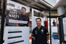 A student stands next to a poster about his Work Integrated Learning experience, featuring his photo and story.