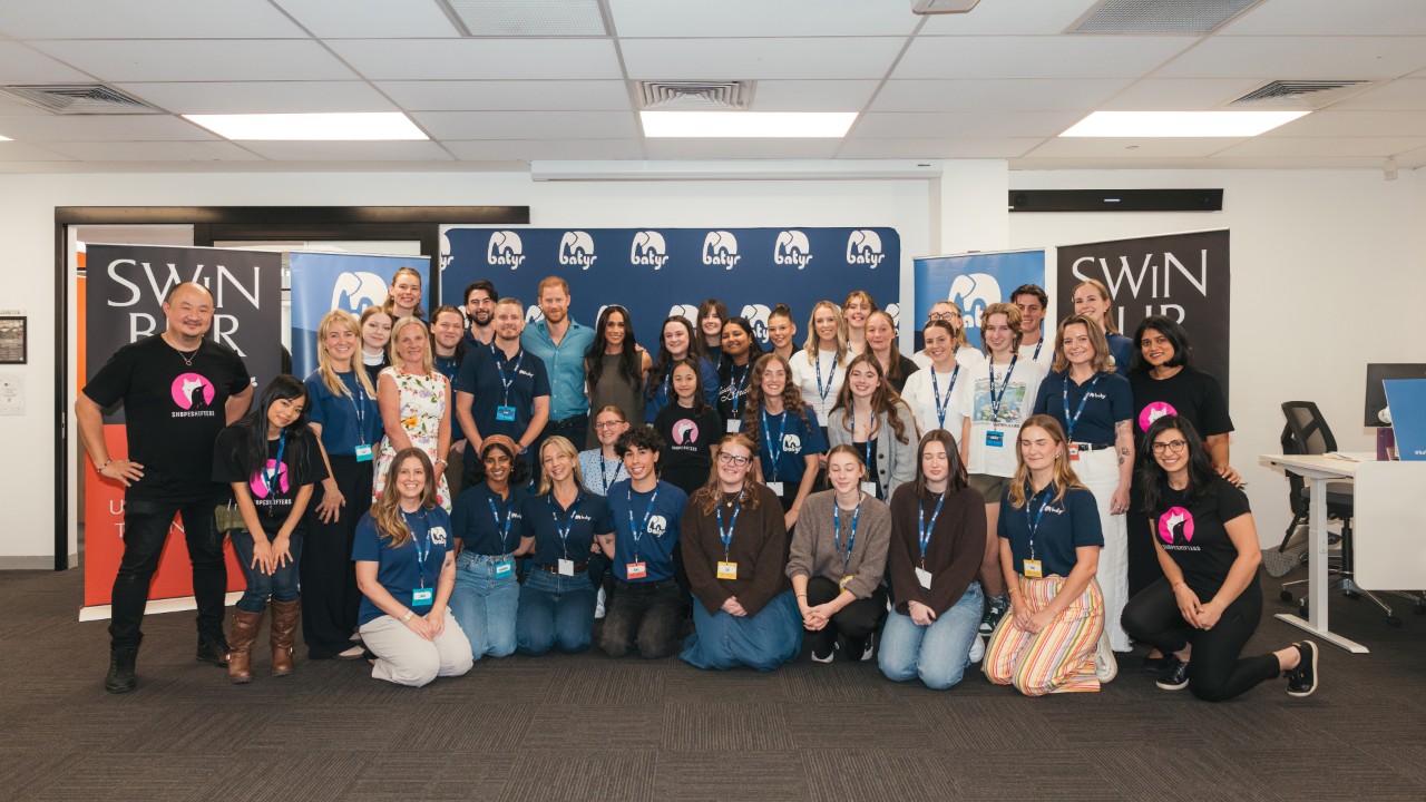 A group photo of batyr student ambassadors, staff, Prince Harry and Meghan on campus in front of batyr and Swinburne banners.