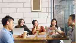 Young people gathered around a cafe table engaging in conversation.