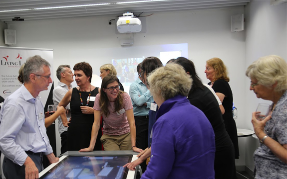 A group of people stand around the table at the launch of the Living Lab