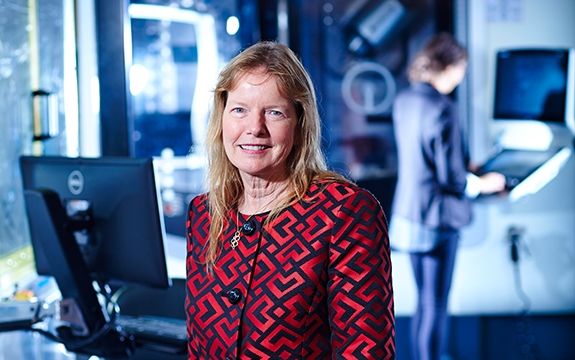 Dr Leonie Walsh standing with machinery in background Dr. Leonie Walsh stands in front of blurred science lab equipment