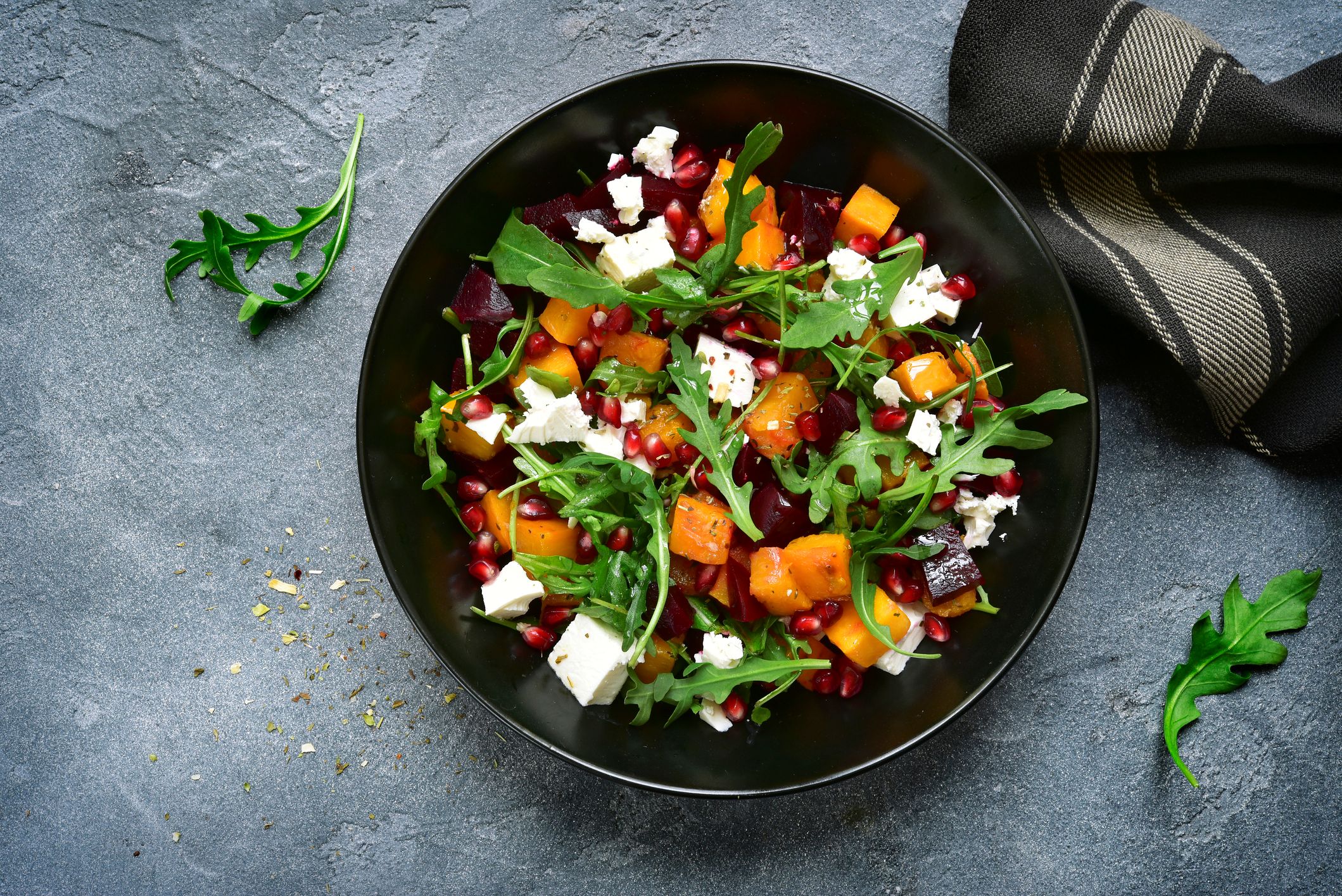 Pumpkin salad with beetroot, arugula and feta cheese in a black bowl over dark grey slate. Pumpkin salad with beetroot, arugula and feta cheese
