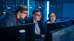 Three IT programmers talking about work, using computers.