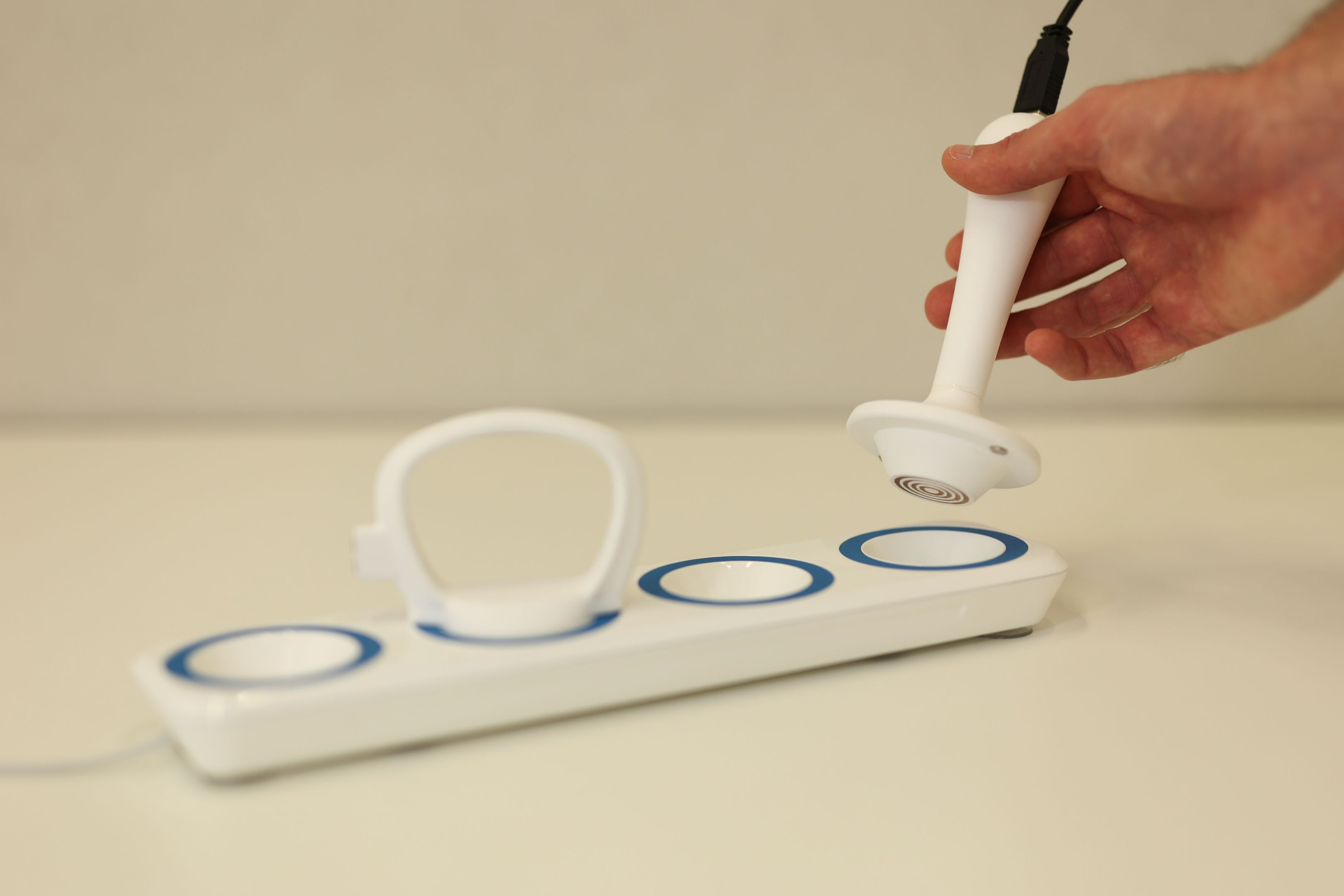 Accessible USB Hub Prototype A white ecteronic panel, similar to a socketboard but with circular magnetic connections rather than power sockets. One round grip connection is already plugged in, while someone connects another connection with a sick style grip