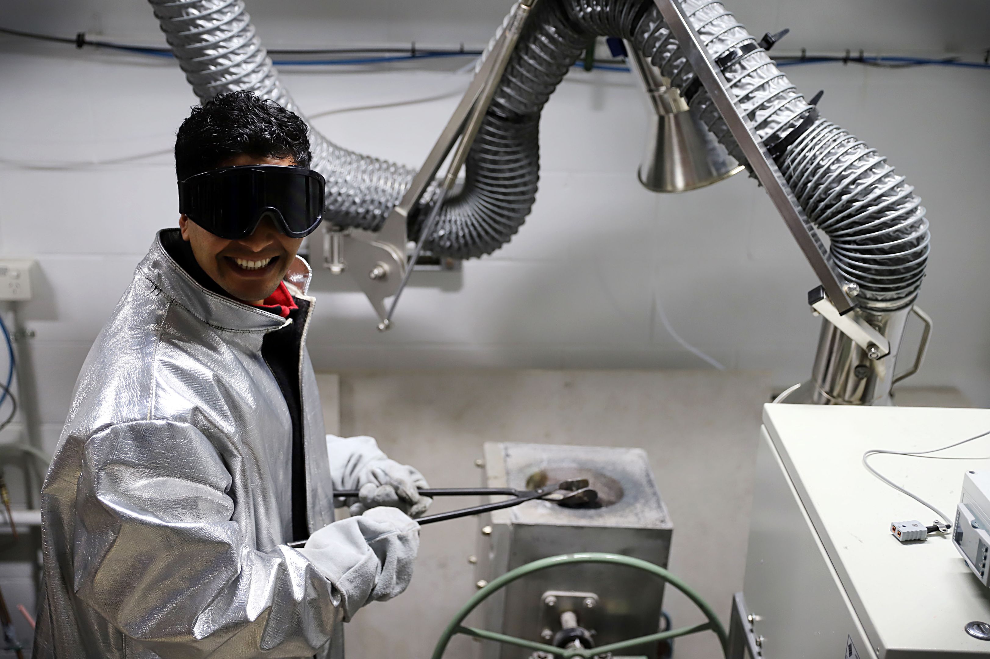 Green steel revolution: How Swinburne researchers are tackling the global climate emergency in steel manufacturing A man in a silver protective jacket and black protective eye goggles folds metal forceps in a scientific research lab