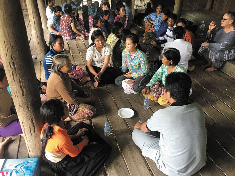 Research Impact Magazine - Cambodia Three groups of people in Cambodia sitting in circles on a wooden floor in discussion