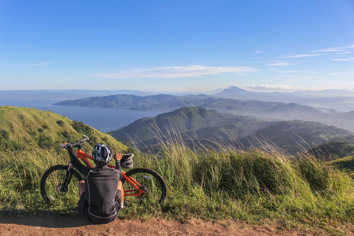 Pick a helmet that fits comfortably A bike rider sitting on the ground next to a bike on top of a hill looking out towards the view of mountains and the sea.
