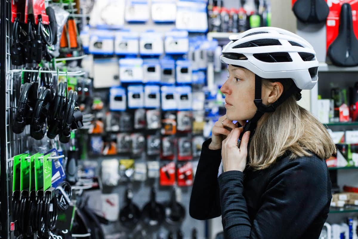 Your helmet should be snug A woman trying on a white bicycle helmet in a bike store.
