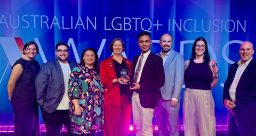 Group of people standing in front of a background that says "Australian LGBTQ+ inclusion", holding a trophy