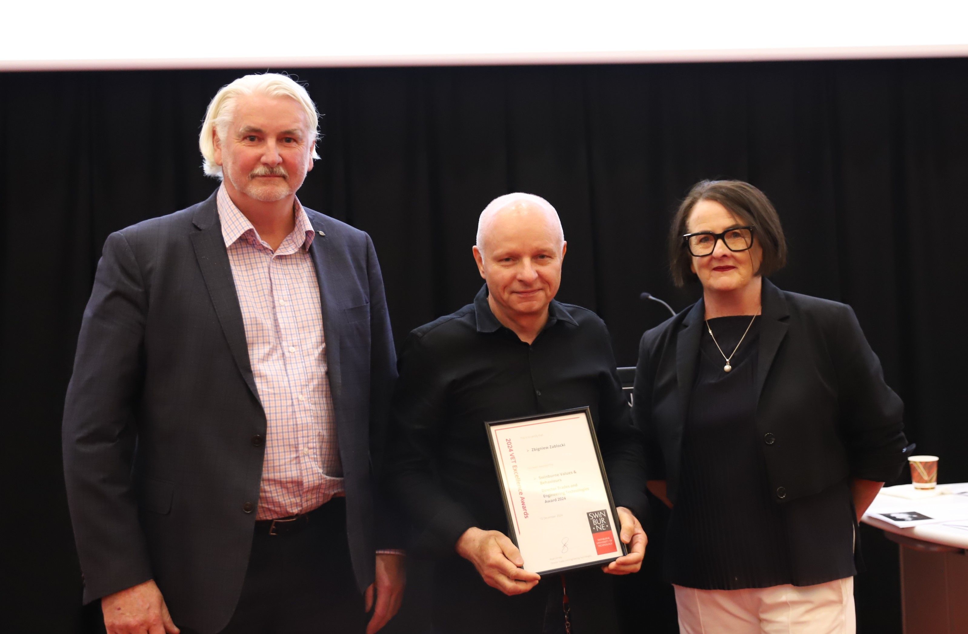 Bryan Ornsby, Zbigniew Zablocki and Madelyn Bolch Three people standing together, man in the middle is holding a frame.