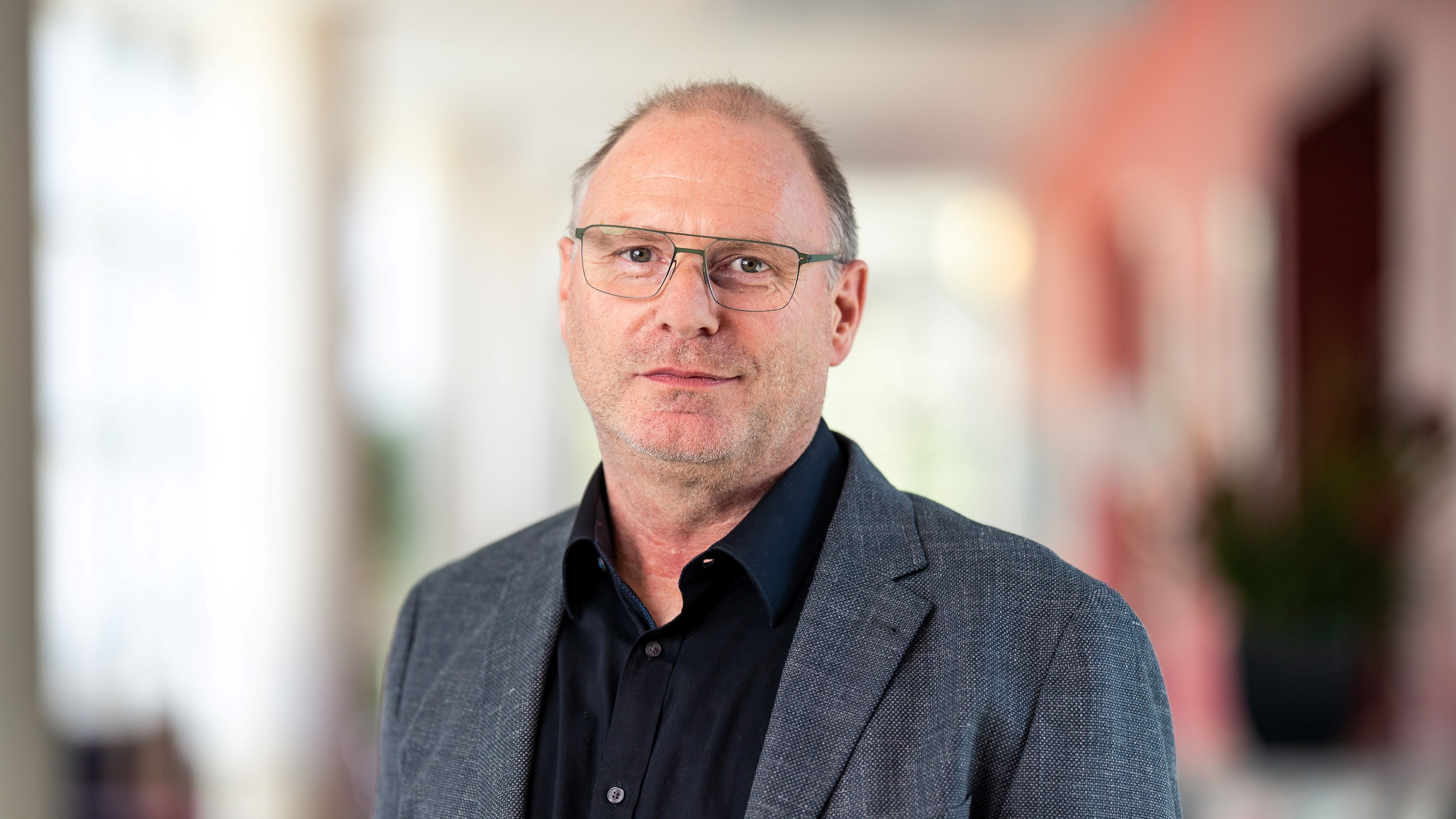 Middle aged man with glasses wearing professional attire, facing the camera with a small smile on his face.