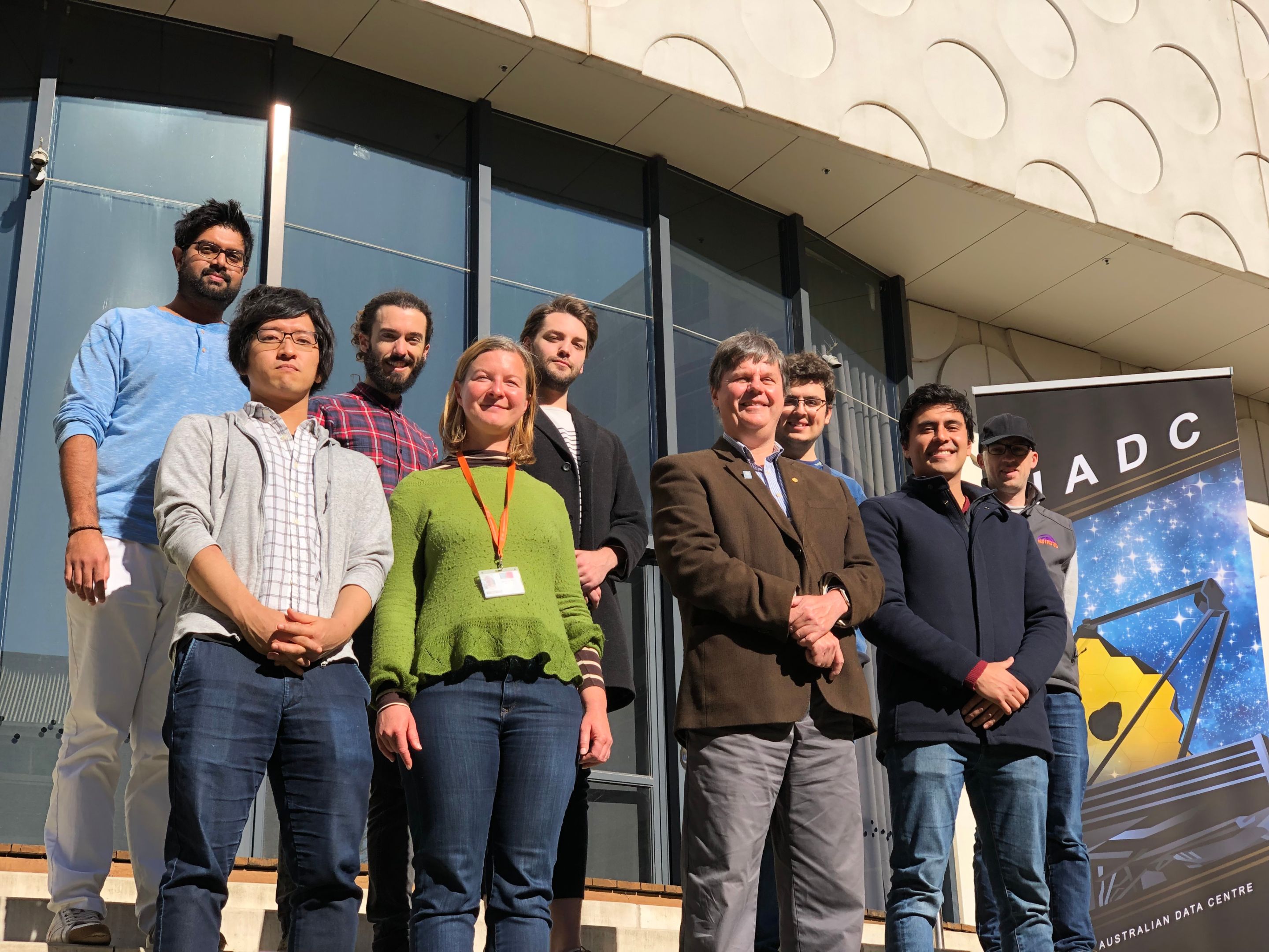 The JWST Laureate science team Eight men and one women from the JWST Laureate science team standing in front of glass windows