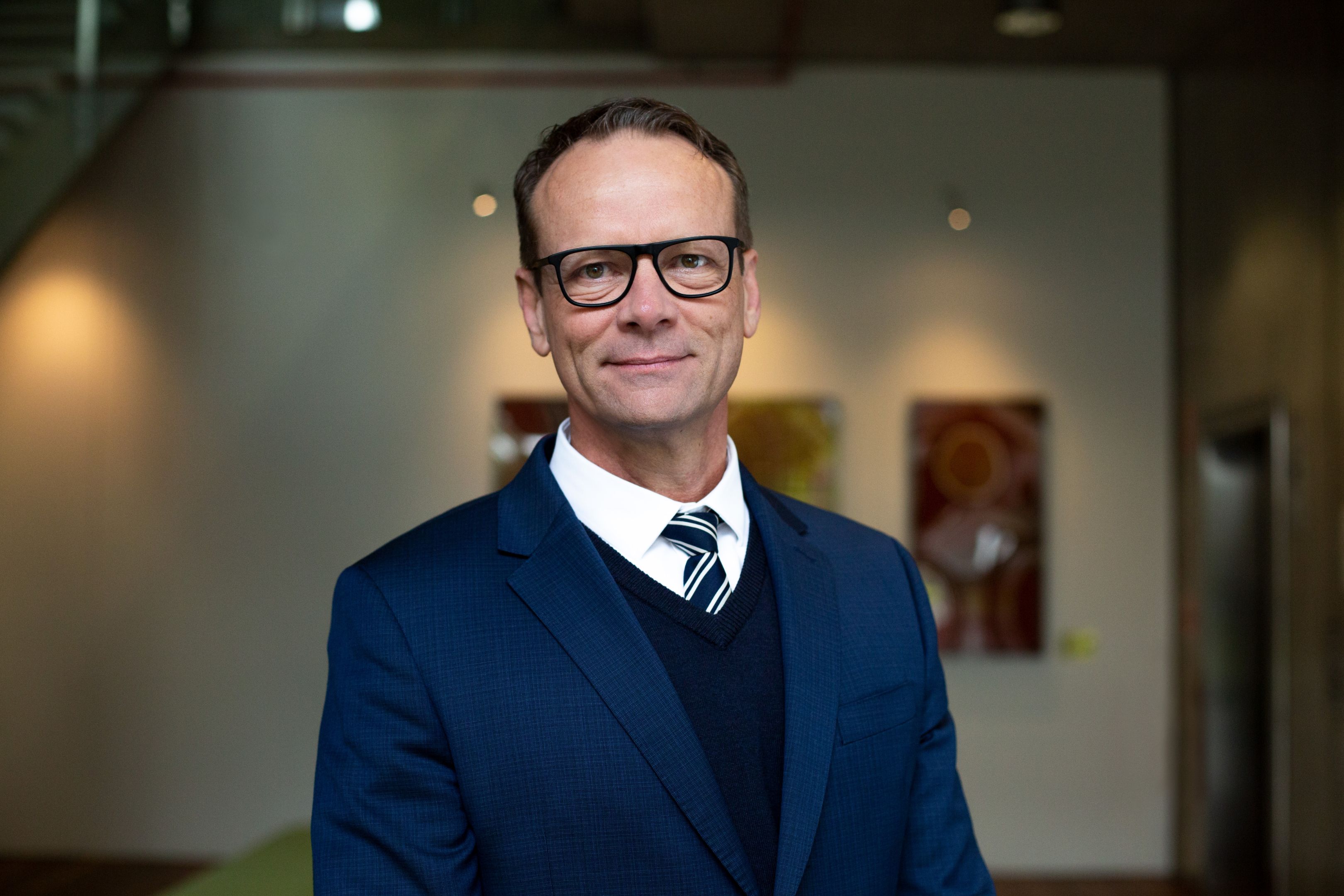 Professor Simon Ridings A male with short hair and glasses wearing a blue suit, white shirt and tie.