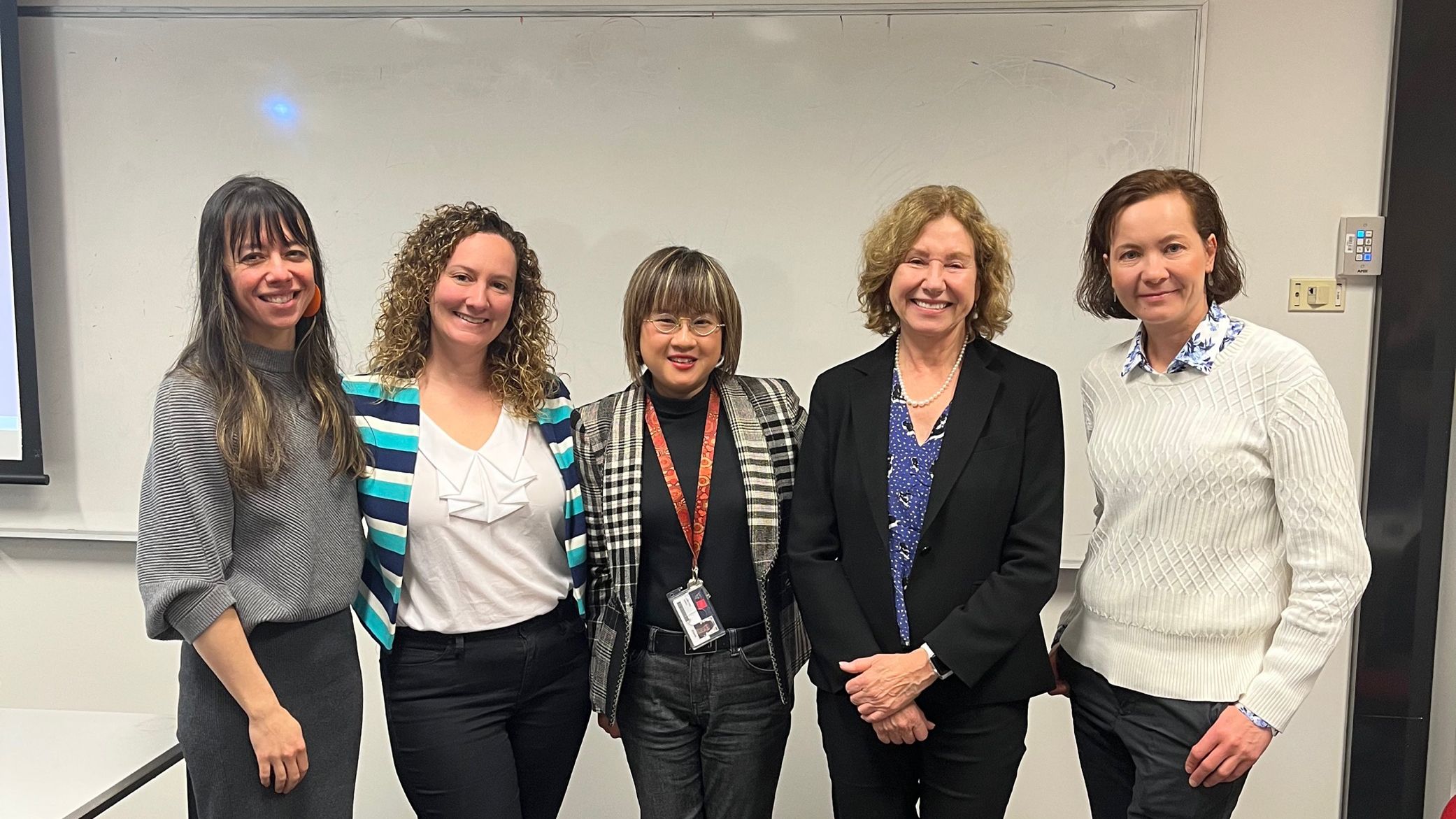 Five professional looking women standing in front of a whiteboard