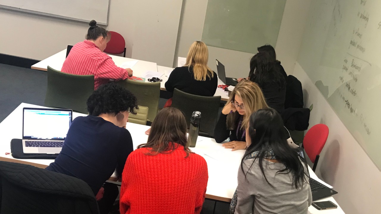 A workshop where women are sitting in groups at tables talking.