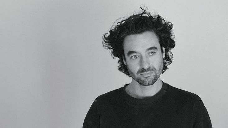 A black and white headshot of Kieran, in a black t-shirt and gazing off camera.