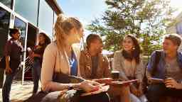 A group of you male and female students happily smiling outdoors.