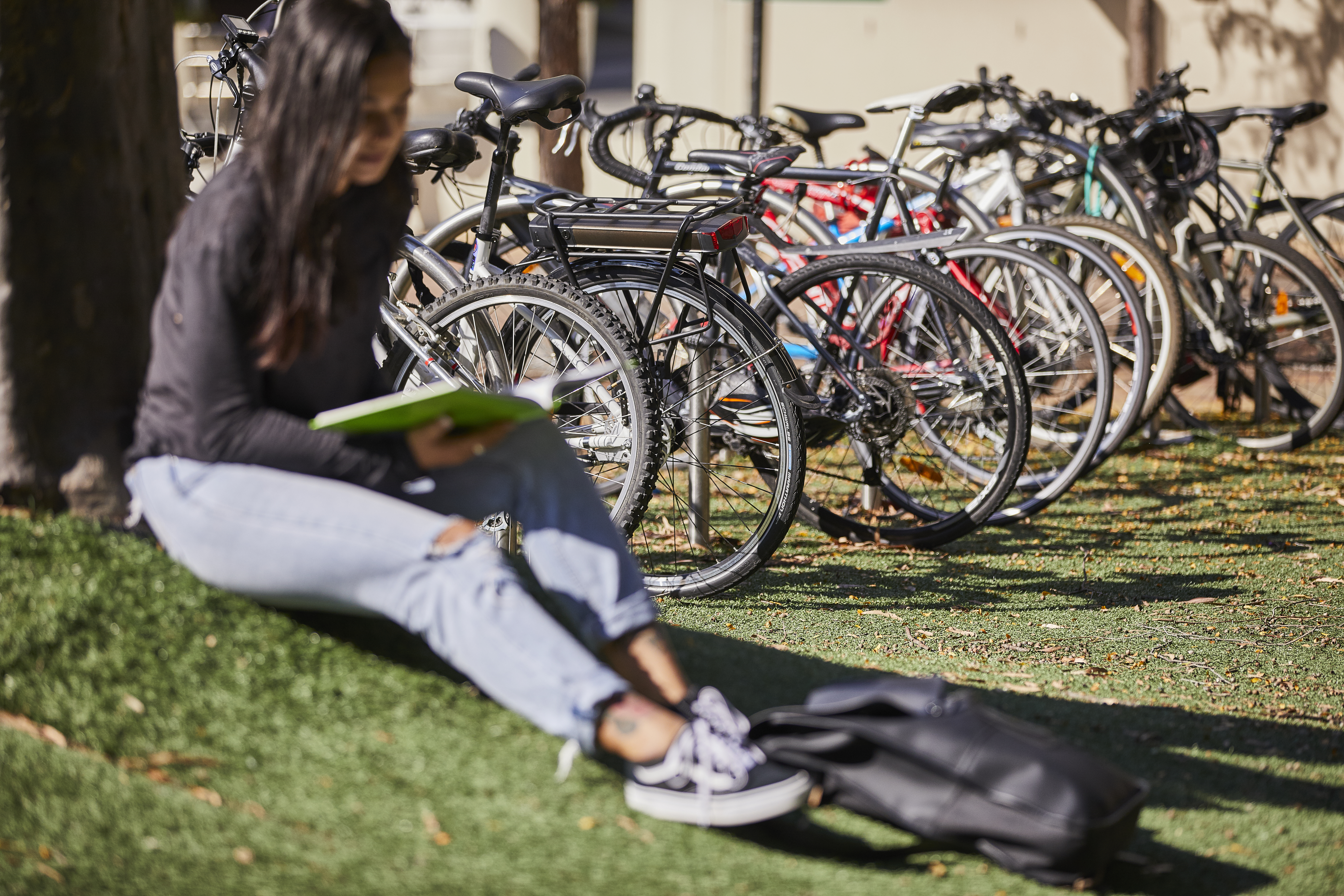 Hawthorn students outside Young woman sits by a tree reading in front of a row of bikes