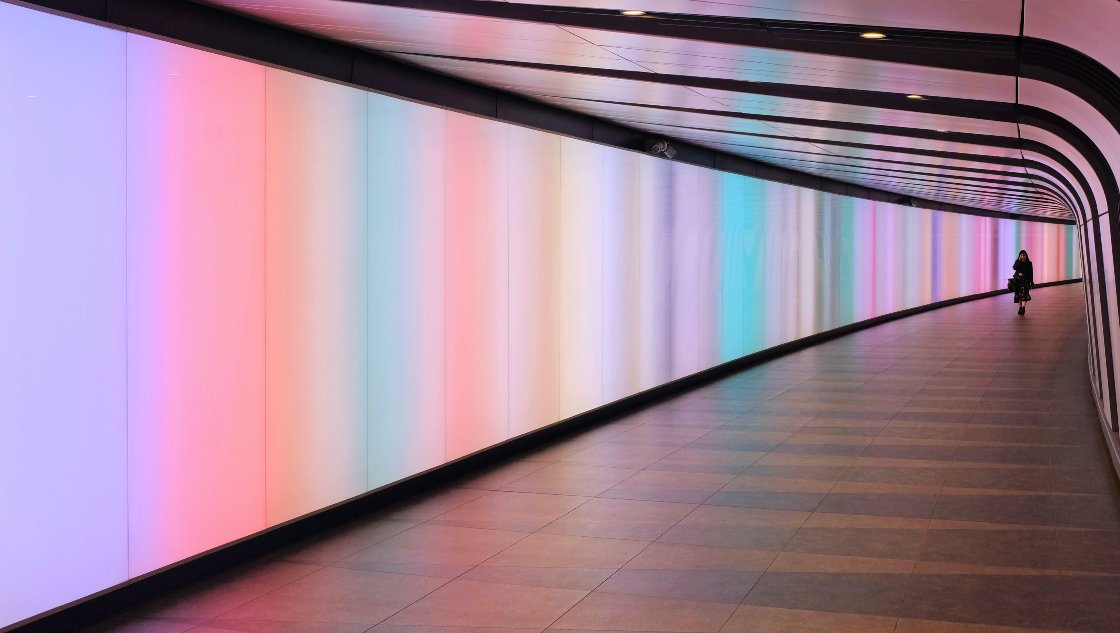 The small silhouette of a woman in a curved, neon-lit underground tunnel 
