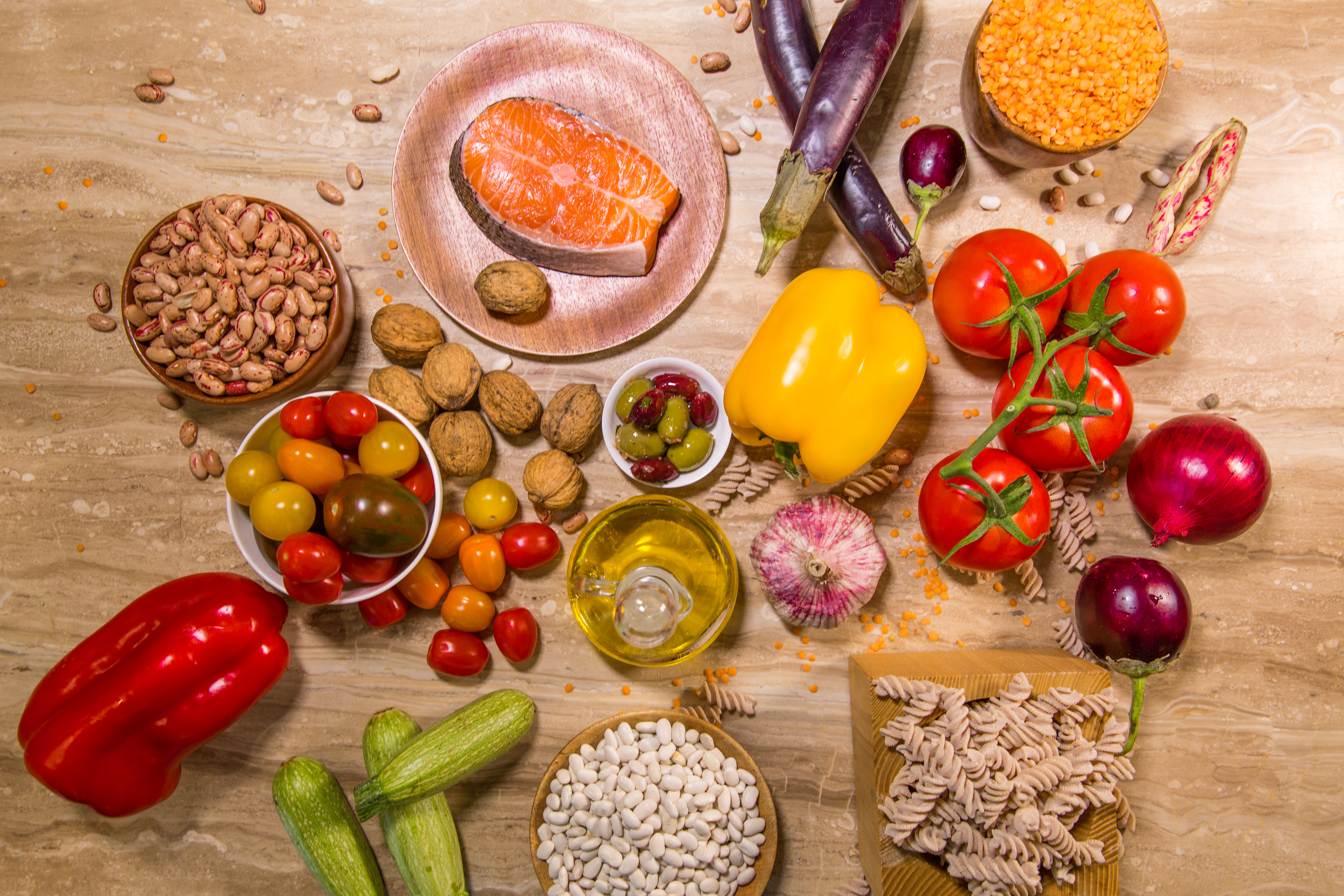A variety of healthy food like tomatoes, nuts, oil, fish and pasta on a wood table.