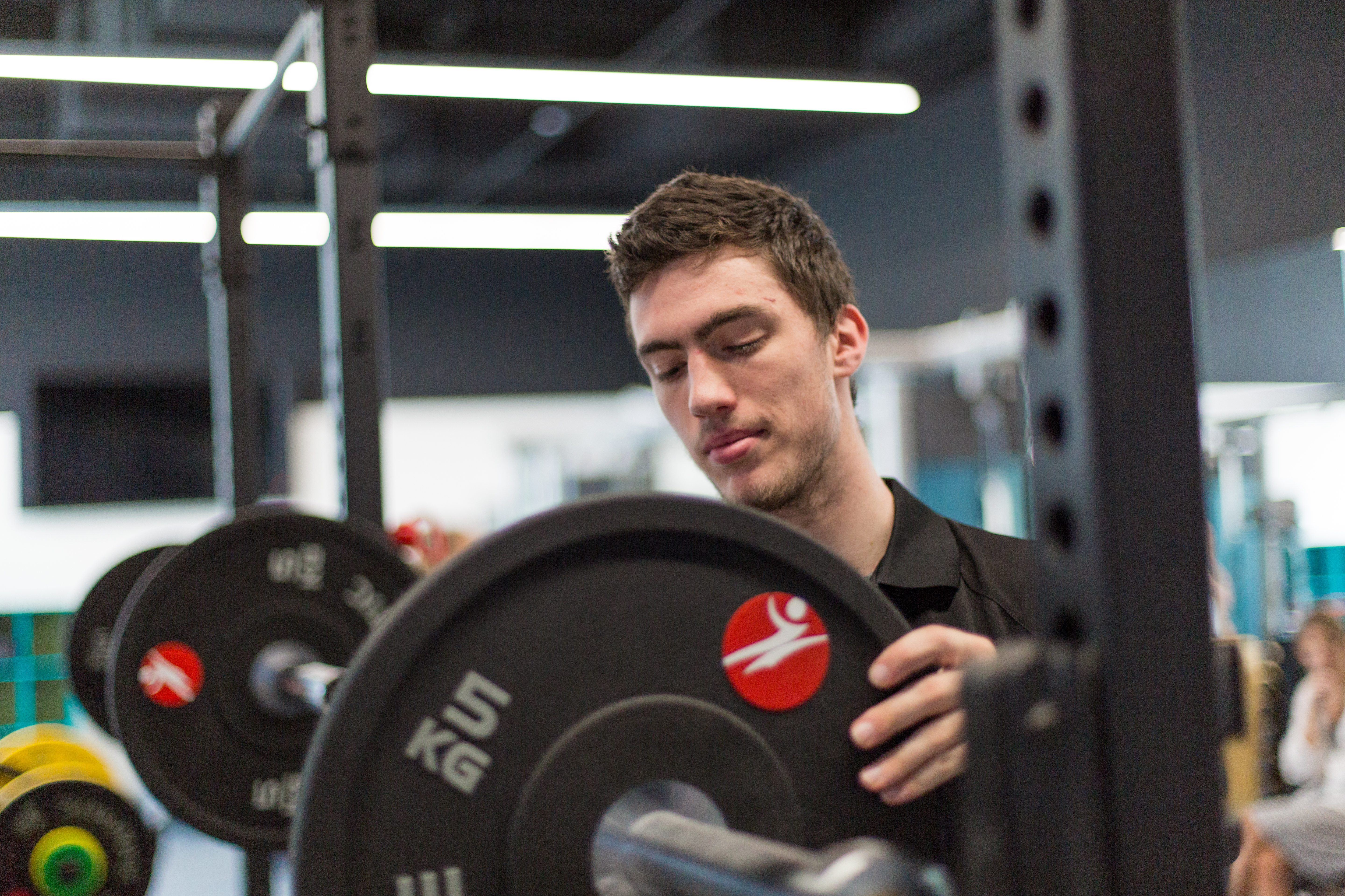 SportsExerciseSci_E6A2988.jpg Male student in the gym lifts a weight onto a bar