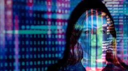 A woman's face is illuminated by a neon digital projection of data