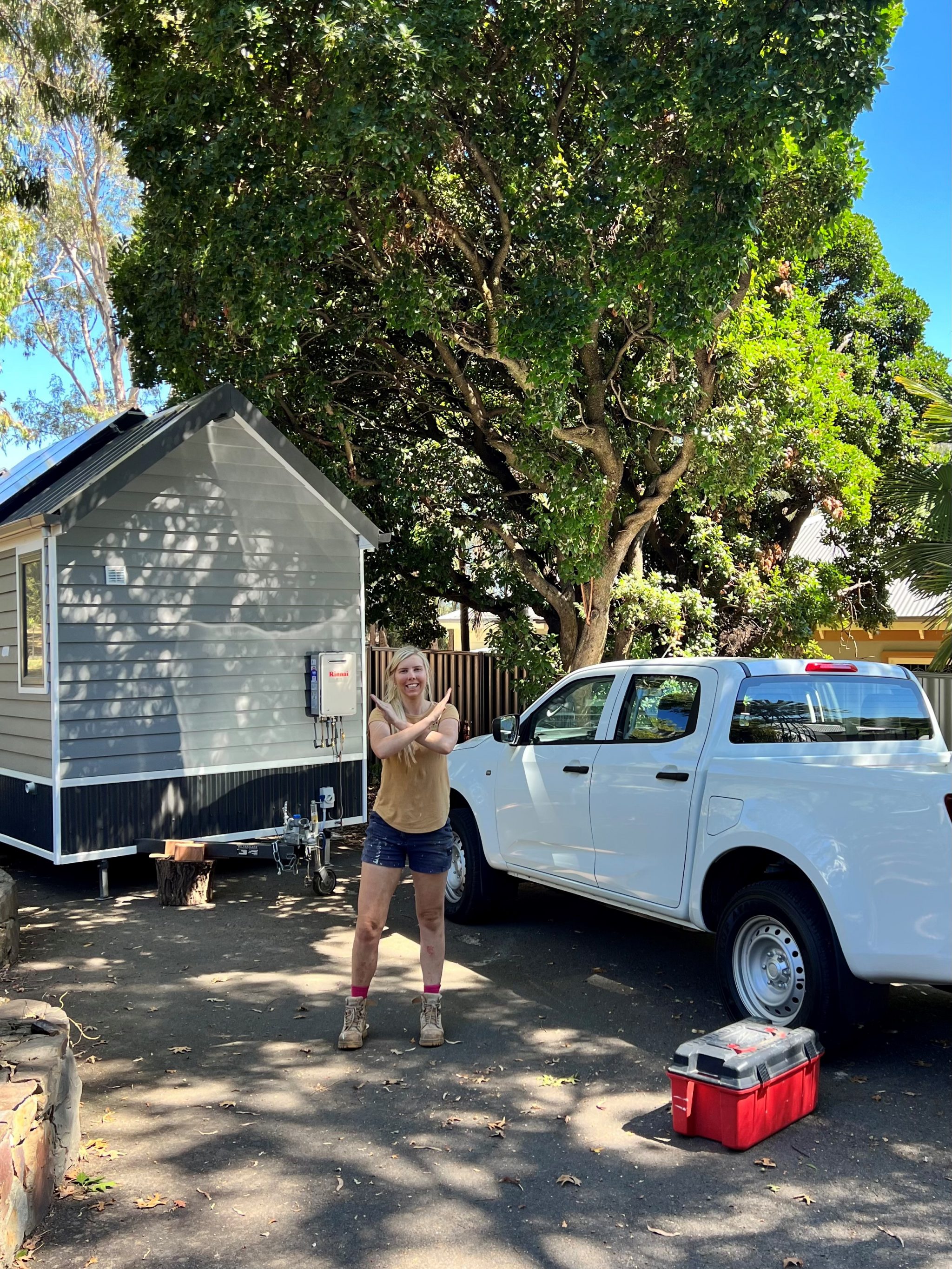 Aimee Stanton International Women's Day Break The Bias Aimee Stanton stands beside her ute and one of her tiny stays homes with her arms crossed in a stance to support breaking the gender bias for international women's day